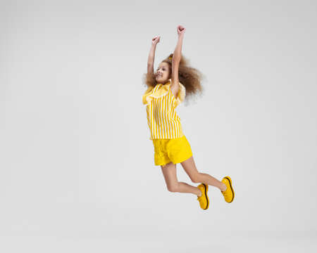Full-length portrait of little active Caucasian preschool girl in bright yellow outfit and shoes jumping isolated over white backgroundの写真素材