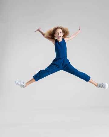 One little Caucasian cute girl in blue stylish jumpsuit jumping high and having fun isolated over white studio background.の写真素材