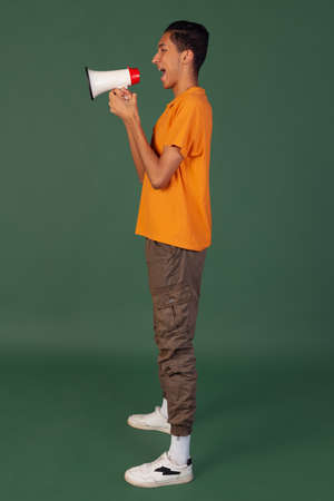 Portrait of young man, student in casual clothes posing isolated on green vintage studio backgroud. Human emotions concept.の写真素材