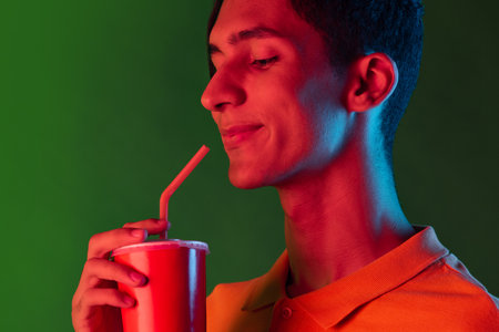 Close-up portrait of young smiling man, student posing isolated on green studio backgroud in neon light. Human emotions concept.の写真素材