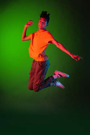 Portrait of young man, student in casual clothes jumping isolated on green vintage studio backgroud. Human emotions concept.の写真素材