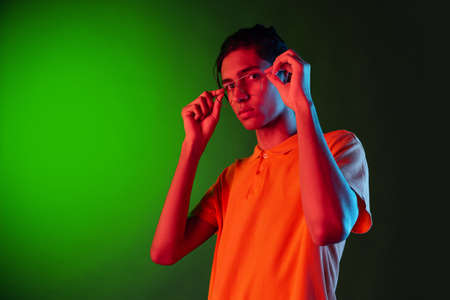 Close-up portrait of young man, student posing isolated on green studio backgroud in neon light. Human emotions concept.の写真素材