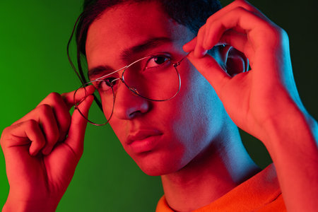 Close-up portrait of young man, student posing isolated on green studio backgroud in neon light. Human emotions concept.の写真素材