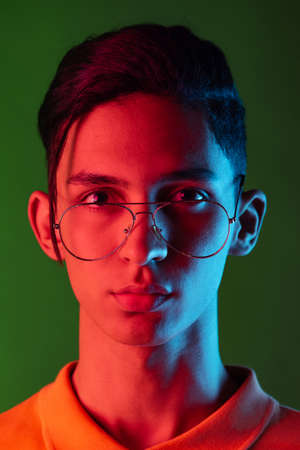 Close-up portrait of young man, student posing isolated on green studio backgroud in neon light. Human emotions concept.の写真素材