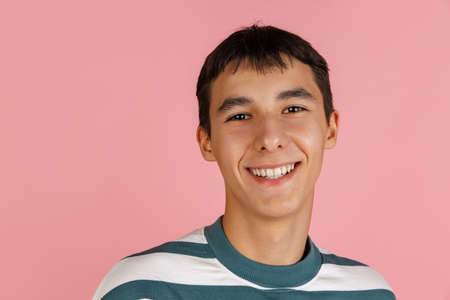 Portrait of young man, student or boy in casual clothes smiling isolated on pink studio backgroud. Human emotions concept.の写真素材