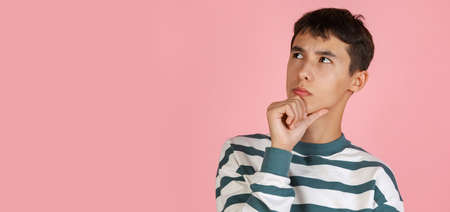 Portrait of young man, student or boy in casual clothes isolated on pink studio backgroud. Human emotions concept.の写真素材