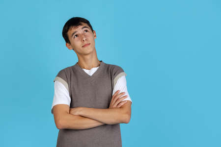 Portrait of young man, student or boy in casual clothes isolated on blue studio backgroud. Human emotions concept.の写真素材