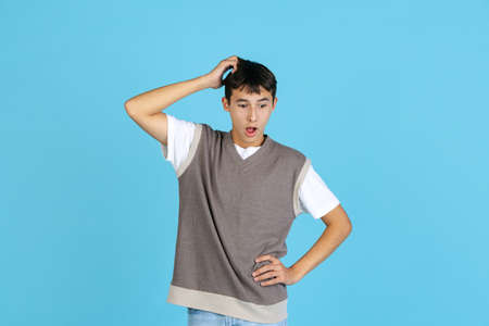 Portrait of young man, student or boy in casual clothes isolated on blue studio backgroud. Human emotions concept.の写真素材