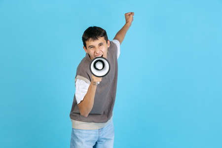 Portrait of young man, student or boy in casual clothes isolated on blue studio backgroud. Human emotions concept.の写真素材