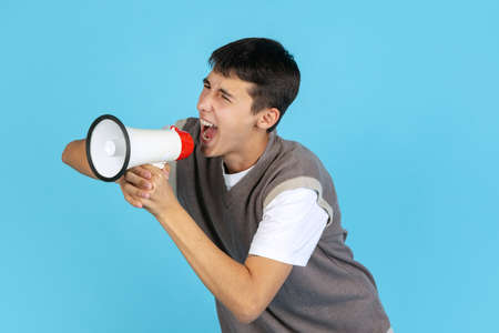 Portrait of young man, student or boy in casual clothes isolated on blue studio backgroud. Human emotions concept.の写真素材
