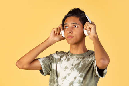 Portrait of young handsome boy, student in casual clothes listening to music isolated on yellow studio backgroud. Human emotions concept.の写真素材
