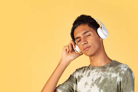 Portrait of young handsome boy, student in casual clothes listening to music isolated on yellow studio backgroud. Human emotions concept.の写真素材