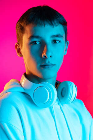 Portrait of young serious boy, student or teen looking at camera isolated on magenta studio...