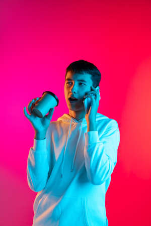 Studio shot of young boy, student, teen in casual clothes using phone isolated on magenta backgroud in neon light.の写真素材