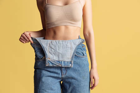 Portrait of young beautiful slim woman in blue jeans jumpersuit posing isolated over yellow studio background. Weight Loss concept.の写真素材