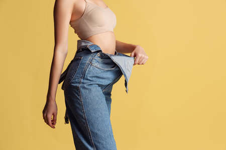 Portrait of young beautiful slim woman in blue jeans jumpersuit posing isolated over yellow studio background. Weight Loss concept.の写真素材