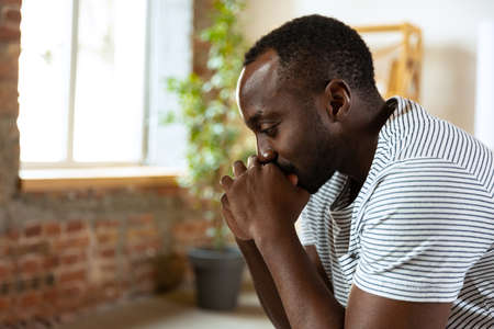 Portrait of young sad african man sitting and thinking about personal problems. Side viewの写真素材