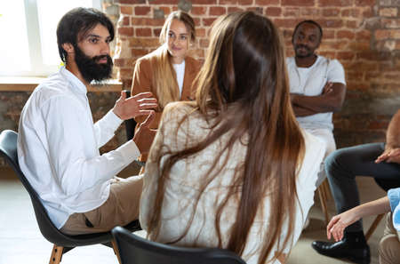 Young multiethnic people, men and woman sitting together, talking, communicate at psychological support group, indoors.の写真素材