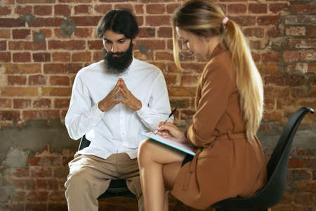Meeting with psychologist. Young woman, consultant helps sad man cope with depression, despair, problems in lifeの写真素材