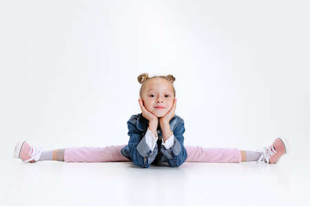 Portrait of little Caucasian cute girl in stylish outfit sitting in a twine on floor isolated over...