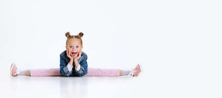 Portrait of little Caucasian cute girl in stylish outfit sitting in a twine on floor isolated over white studio background.の写真素材