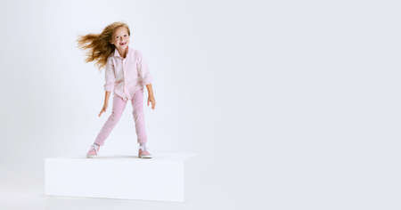 Full-length portrait of smiling girl in casual clothes standing on big box isolated on white studio background. Happy childhood concept.の写真素材