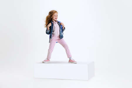 Full-length portrait of smiling girl in casual clothes standing on big box isolated on white studio background. Happy childhood concept.の写真素材