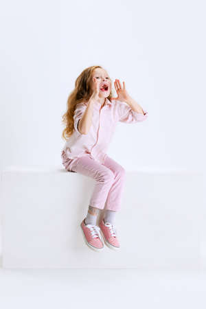 Studio shot of cute beautiful girl with long silk hair in casual clothes sitting on big box isolated on white background.の写真素材