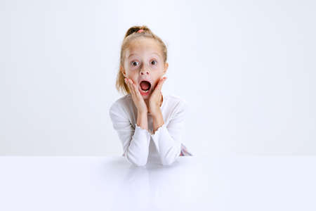 Portrait of beuatiful school girl sitting and looking at camera isolated on white background. Happy childhood, educationの写真素材