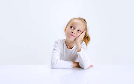 Portrait of beuatiful school girl sitting and looking at camera isolated on white background. Happy...