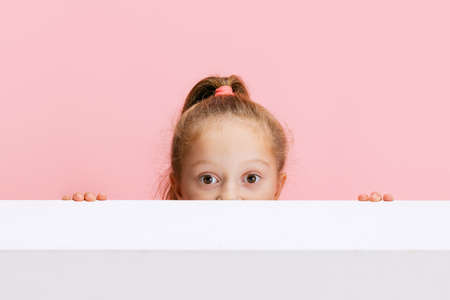 Portrait of funny cute beautiful girl peeping out from behind the wall isolated on pink background.の写真素材