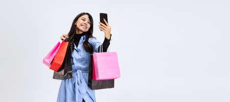 One beautiful young girl shopping while black friday sales. Model with lots of bags, colorful bright packages isolated over white studio background.の写真素材
