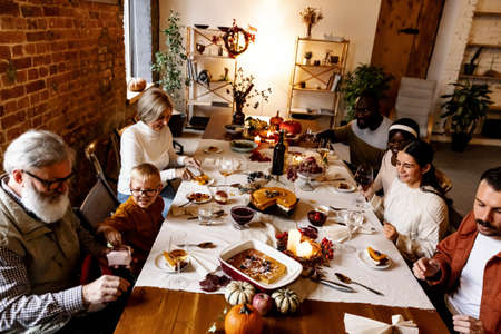 Happy Thanksgiving dinner party with family and friends with turkey and holiday traditional food, dishes on table.の写真素材