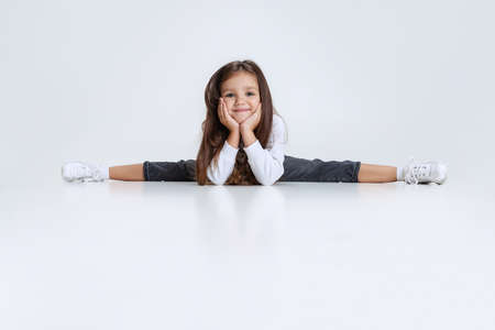 Portrait of little Caucasian cute girl wearing hoodie with jeans sitting on a twine and having fun isolated over white studio background.の写真素材