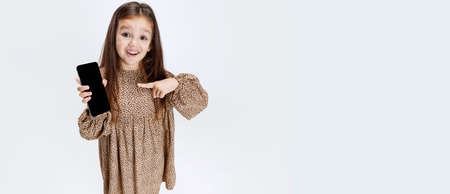 Flyer with little cute smiling preschool beautiful girl showing phone screen isolated over white studio background.の写真素材