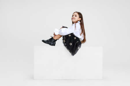 Studio shot of cute little girl in casual clothes sitting on big box isolated on white background.の写真素材