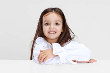 Portrait of beuatiful school girl sitting and looking at camera isolated on white background.の写真素材