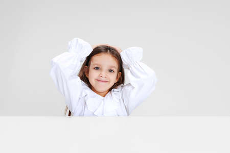 Portrait of beuatiful school girl sitting and looking at camera isolated on white background.の写真素材