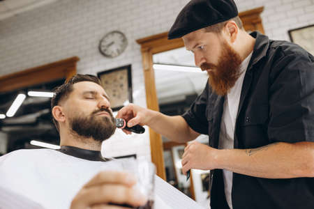 Professional barber, clipper cutting, shaving beard of regular customer at barbershop. Beauty, selfcare, style, fashion and male cosmetics concept.の写真素材