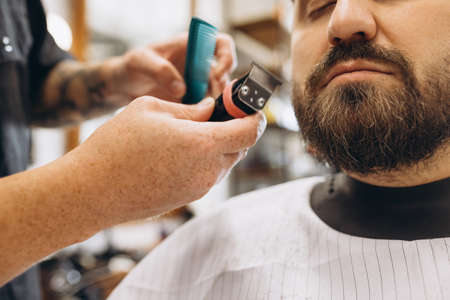 Professional barber, clipper cutting, shaving beard of regular customer at barbershop. Beauty, selfcare, style, fashion and male cosmetics concept.の写真素材