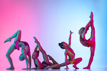 Group of beautiful flexible rhythmic gymnastics artists, girls in sport event isolated on gradient pink blue studio background in neon lightの写真素材