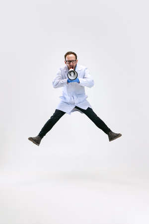 One excited man, chemist, doctor jumping and shouting at megaphone isolated on white background.の写真素材