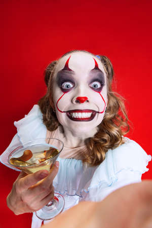 Halloween spooky theme. Close-up beautiful artistic girl in halloween make up looking at camera isolated over red backgroundの写真素材