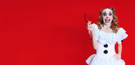 Halloween spooky theme. Portrait of beautiful artistic girl in halloween make up and costume of dancing clown isolated over red backgroundの写真素材