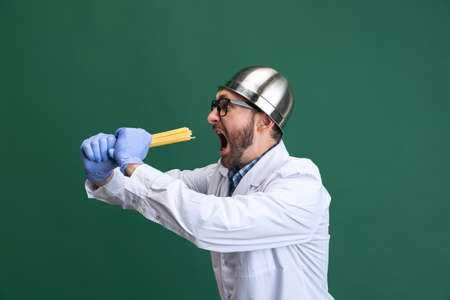 Comic portrait of young man wearing white gown and protective gloves having fun isolated on green background.の写真素材