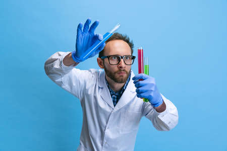 Close-up young chemist, doctor conducts chemical research isolated on blue background. Concept of pharmacology.の写真素材