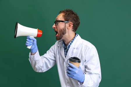 Portrait of young man wearing white gown and protective gloves having fun isolated on green background.の写真素材