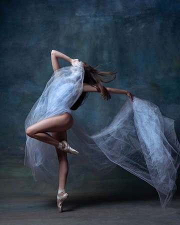 Portrait of young and flexible ballet dancer, ballerina dancing isolated on dark vintage studio background. Art, motion, action concept.の写真素材