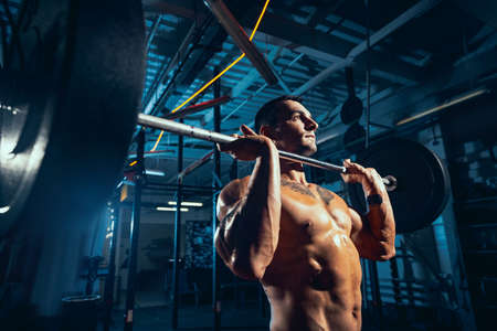Close-up young man, muscled athlete, bodybuilder training alone at sport gym, indoors. Concept of...