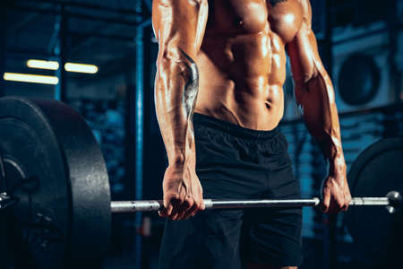 Close-up young man, muscled athlete, bodybuilder with heavy barbell at sport gym, indoors. Concept of sport, activity, healthy lifestyleの写真素材